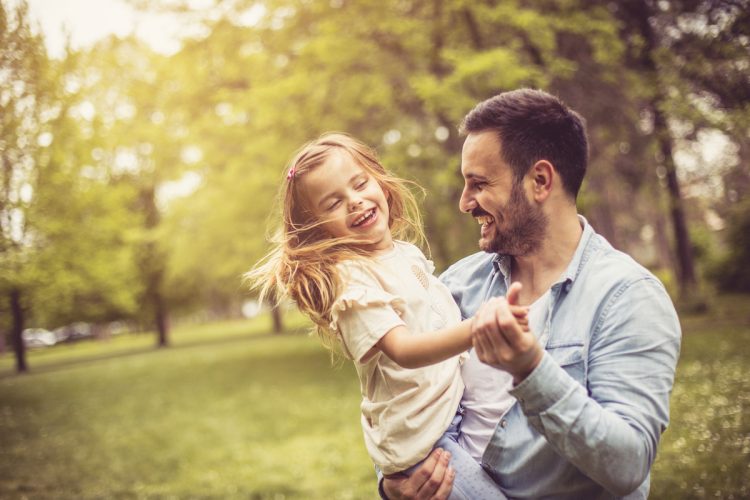 Father and daughter at park dancing and holding hands.